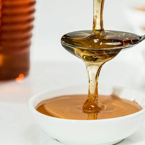 Delicious honey pouring slowly from a spoon into a white bowl, highlighting its golden hue and viscosity.