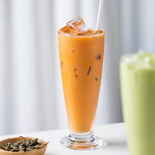 Tall glass of iced Thai tea with tapioca pearls, served with a straw on a white background.