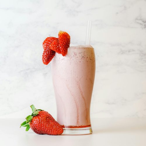 Delicious and creamy strawberry milkshake garnished with fresh berries on a white marble background.