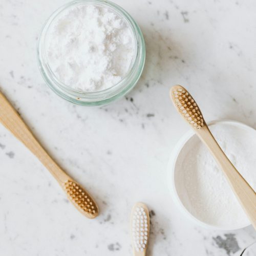 From above of glass and plastic jar with white tooth powder near wooden toothbrushes on marble table with grey lines and crack