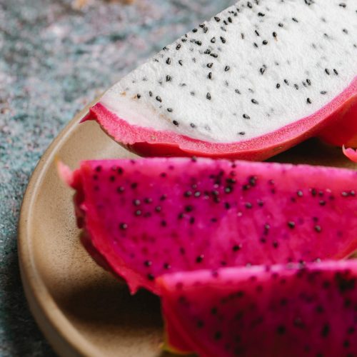 Pieces of ripe tasty dragon fruit with pink and white flesh served on round plate on marble table in kitchen