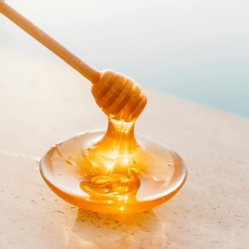 Golden honey flowing from a wooden dipper onto a glass plate, captured in warm daylight.