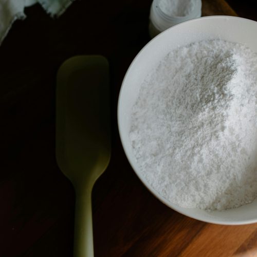 A close-up view of a bowl of flour with baking utensils on a wooden surface.