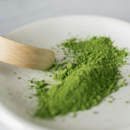 Vibrant green matcha powder on a ceramic plate with wooden spatula in a minimalist setting.