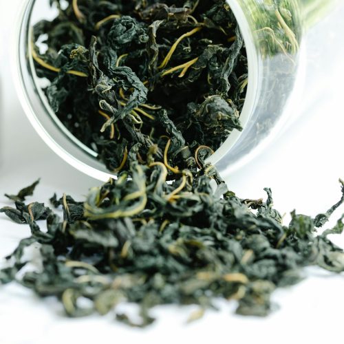 A close-up of dried black tea leaves spilling from a glass jar, showcasing texture and freshness.