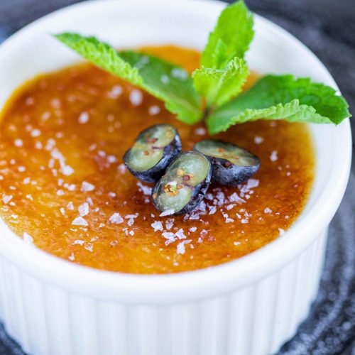 Close-up of a creamy crème brûlée topped with mint and berries.